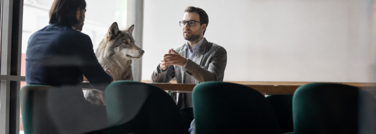 neuvottelupöydän ääressä kaksi miestä pitää työhaastattelua, mutta pöydässä istuu myös susi